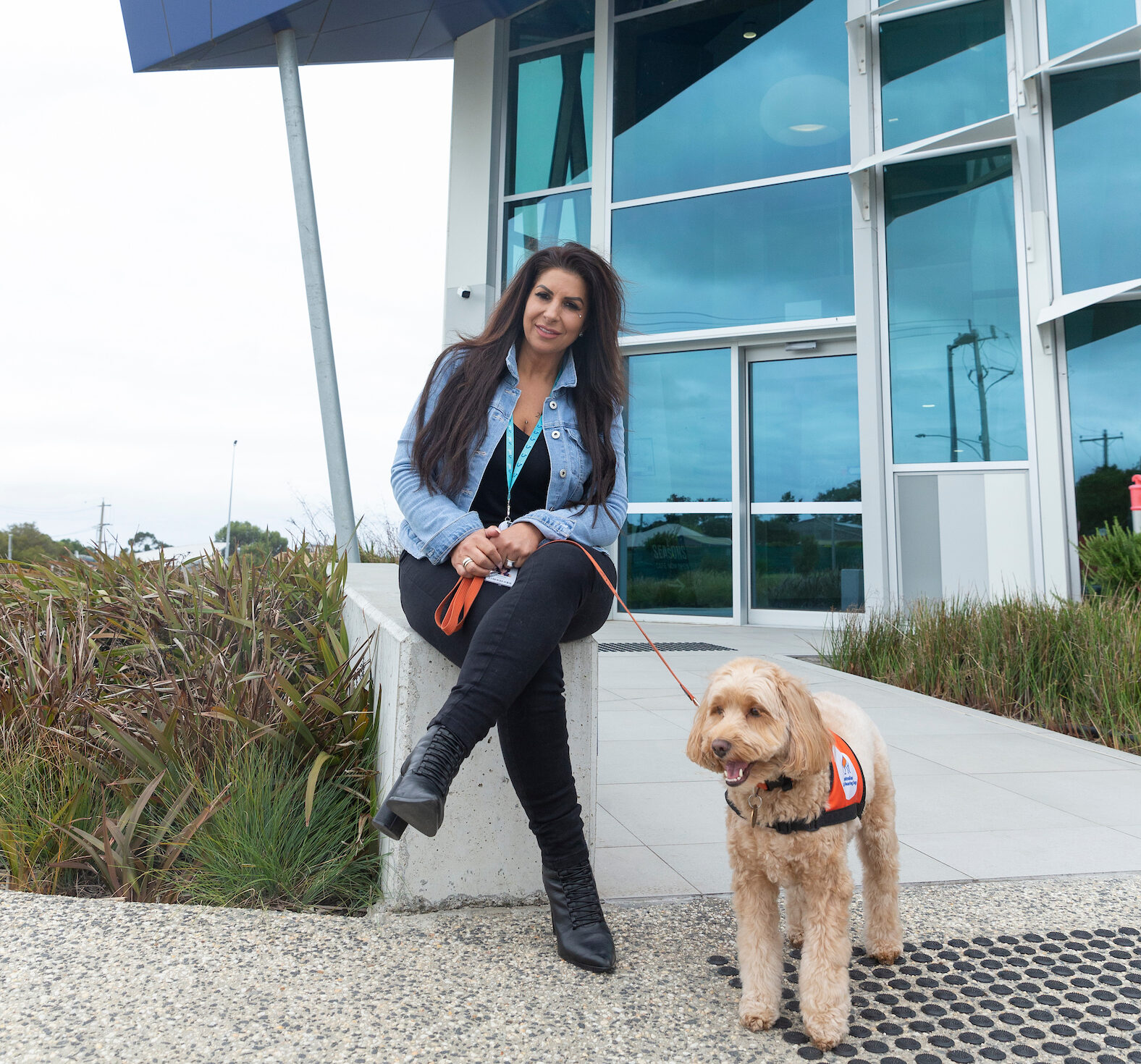 genU employee Danielle walking outside the genu Support Hub in Highton, Geelong with her Lions hearing dog, Honey who is a mini labradoodle.