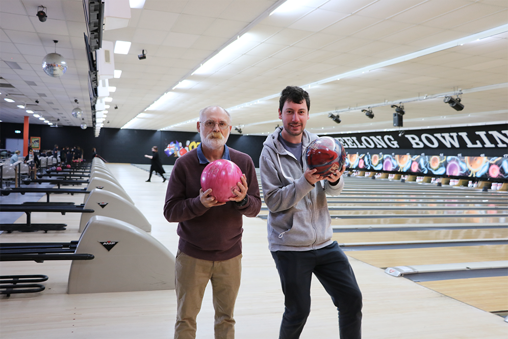 Two people standing posing for the camera while holding bowling balls in a bowling alley