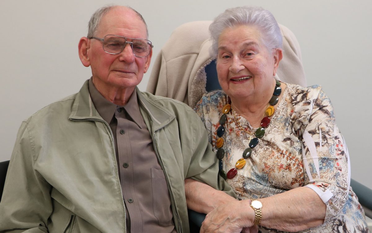 Aged care couple seated smiling with arms linked