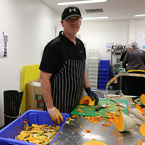 A man standing in a kitchen wearing a chef uniform. There is pumpkin scraps on the bench.