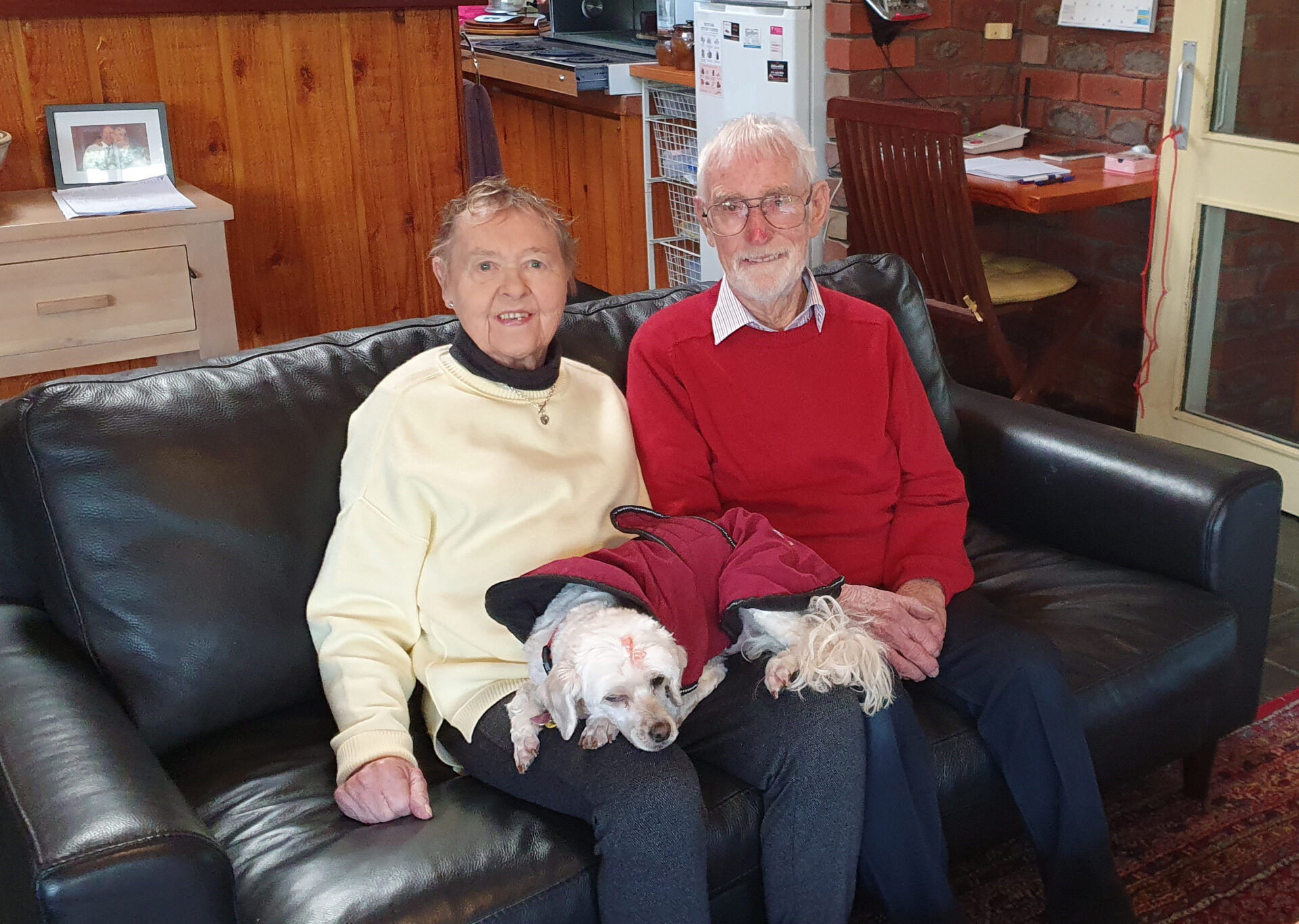 An elderly couple sitting on their couch with their pet dog