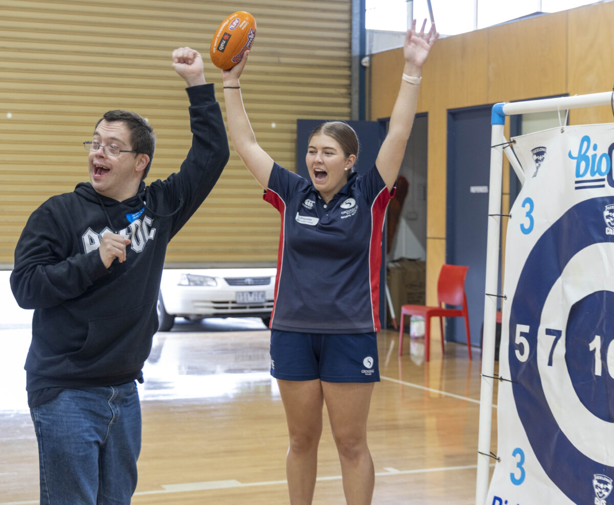 A male genU participant with disability celebrating after hitting the cats themed target in the Handball activity. A female Grovedale College Sports Academy student is pictured behind him with both hands in the air celebrating too.