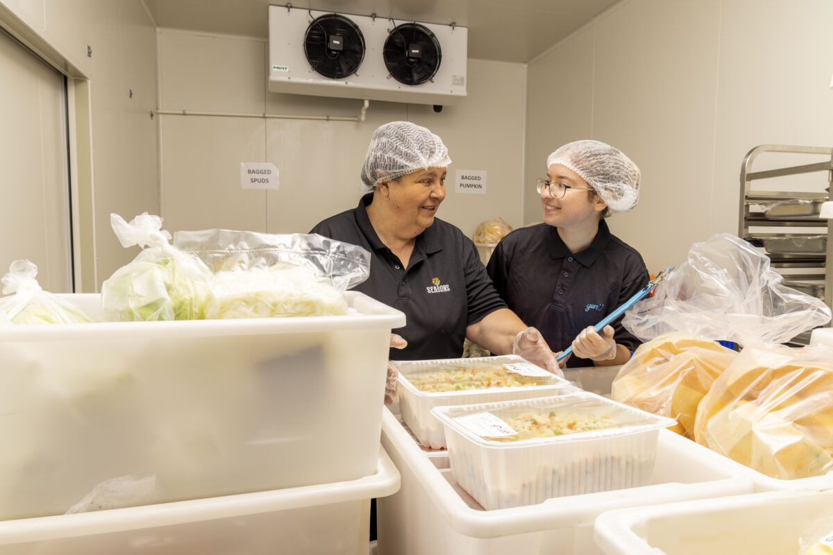 Female supported employee with supervisor organising the processed vegetables in the commercial freezer.