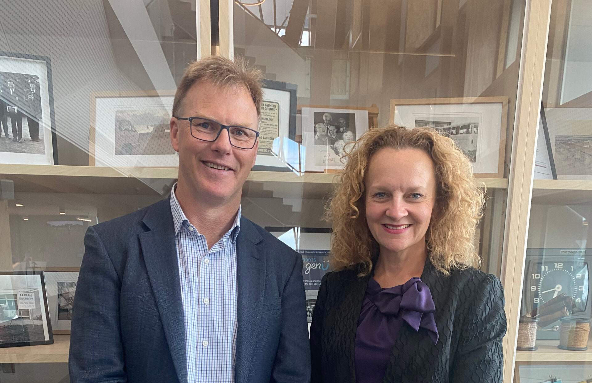 Li-Ve Tasmania CEO, Darren Mathewson stands beside genU CEO, Clare Amies at the genU Support Hub. Darren wears stone coloured pants and a navy jacket and a pale blue shirt. Clare is wearing a black dress and jacket.