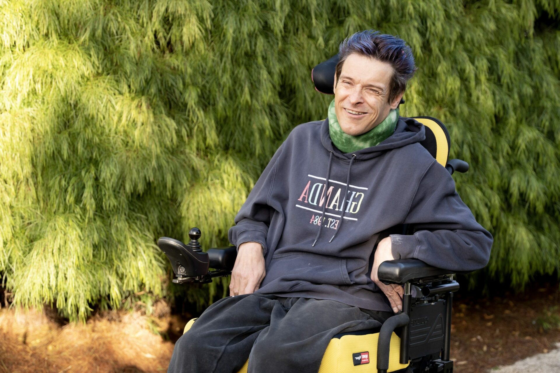 Disability advocate Patrick Eadington in his mobility chair outside with a green hedge in the background.