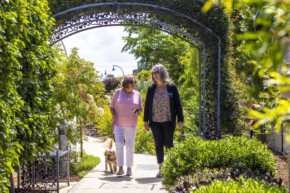 An older woman and a Barwarre Gardens staff member walk through the communal gardens.