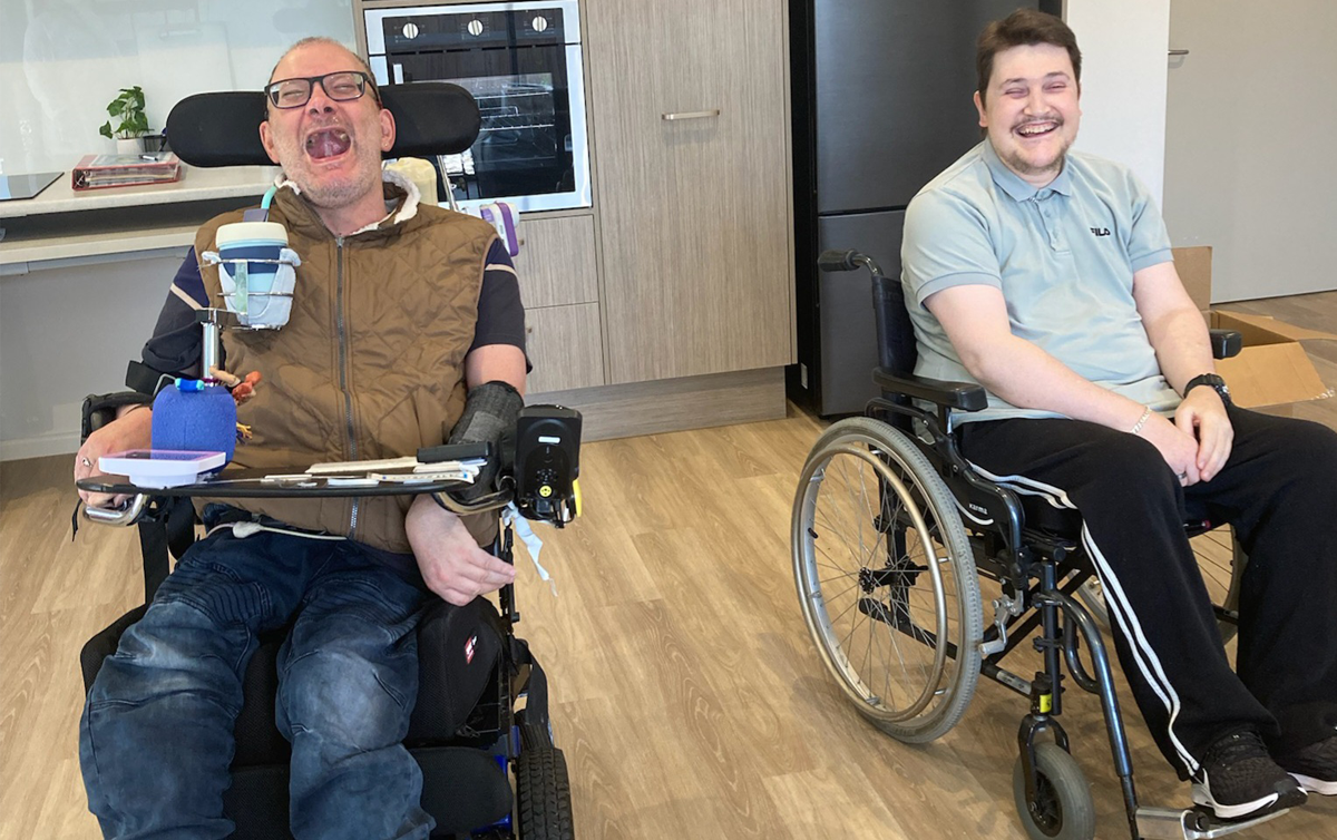 Two men are in wheelchairs, they are smiling as they sit in their new disability accommodation.